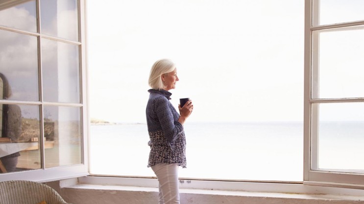 Frau am offenen Fenster mit Blick aufs Meer