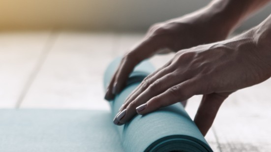 Hände, die eine Yogamatte ausrollen