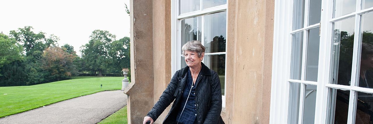 Frau mit Sauerstoffgerät vor Haus