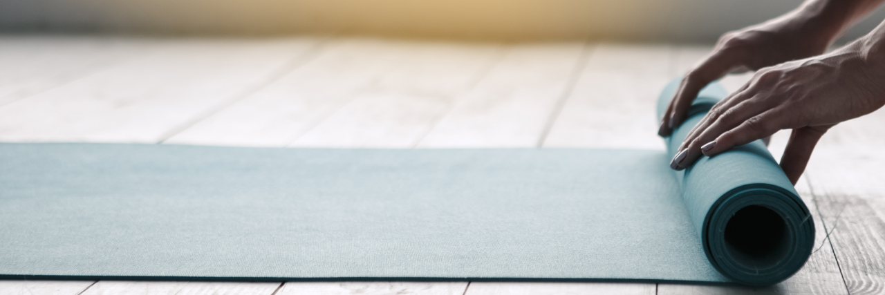 Hände, die eine Yogamatte ausrollen
